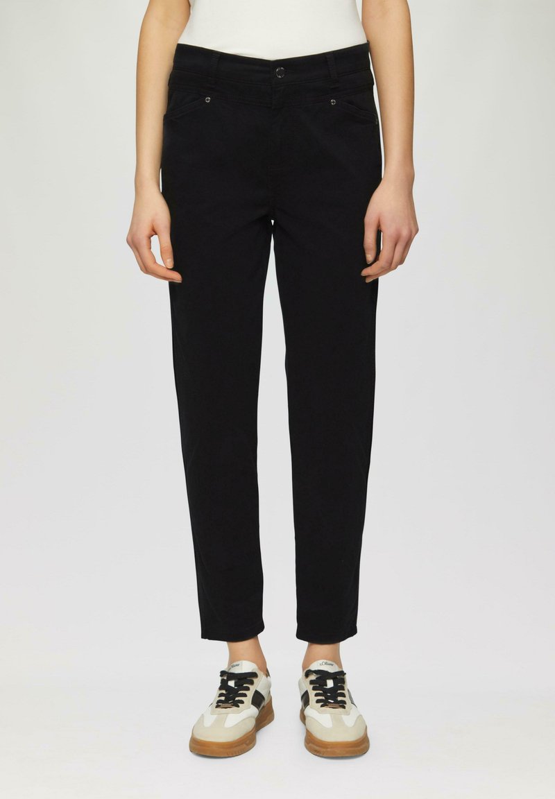 Pantalon noir au design ajusté et fuselé, avec des poches avant et des détails de couture subtils, associé à des baskets de couleur claire.