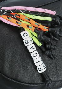 Colorful braided cords in pink, orange, black, and green with textured accents; features white beads spelling "PICARD" and black tips.