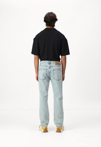 Polo shirt noir à manches courtes, jeans droits bleu clair, baskets jaunes avec semelles texturées, vue de dos.