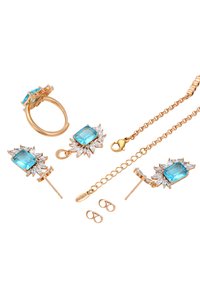 Set di gioielli in tono oro composto da un anello, orecchini e una collana. Il pezzo centrale è una pietra blu quadrata circondata da accenti trasparenti.