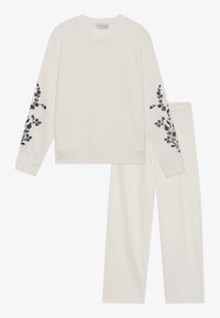 Conjunto de sudadera crema y pantalones a juego, con bordado floral negro en las mangas, tejido suave y cintura elástica para mayor comodidad.