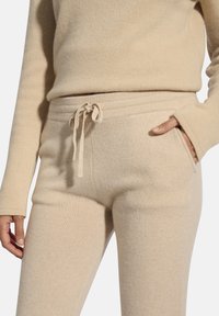 Beige Strick-Sweatpants mit einem Kordelzugbund, Seitentaschen und einer weichen Textur. Kombiniert mit einem passenden Langarmoberteil.