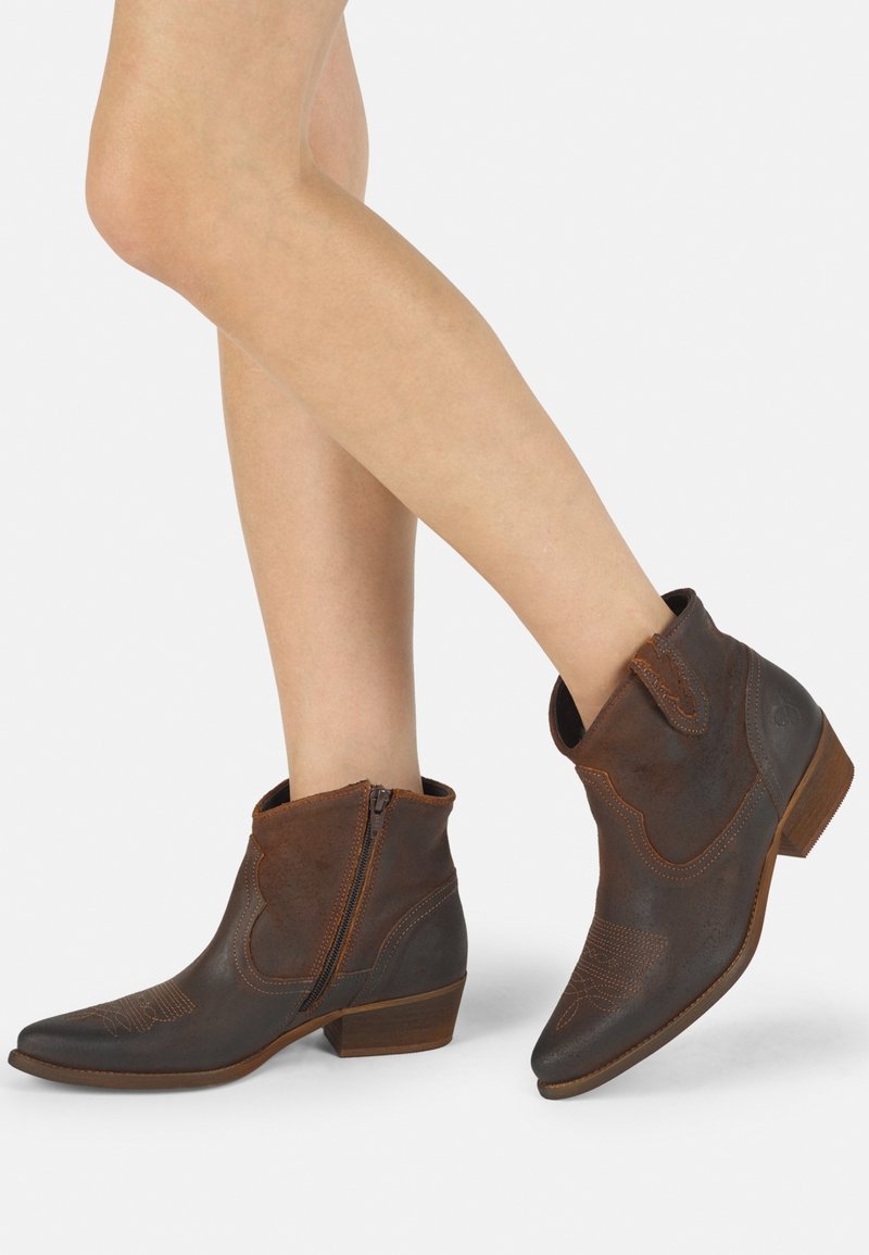 Botas de cuero marrón hasta el tobillo con punta afilada, tacón bajo, cremallera lateral y costura decorativa en la parte delantera. Acabado texturizado con un upper suave.