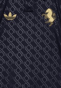 Marineblauw poloshirt met een gestructureerd ruitpatroon. Gouden geborduurd paardenlogo en Adidas trefoil-embleem op de linkerborst.