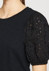 Sort top med korte puffærmer, broderet blomsterdesign og øjelette detaljer. Blød tekstur med en afslappet pasform.