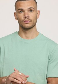 T-shirt en coton vert menthe avec un col rond, des manches courtes et une texture lisse, ne présentant aucun motif ni graphique visible.