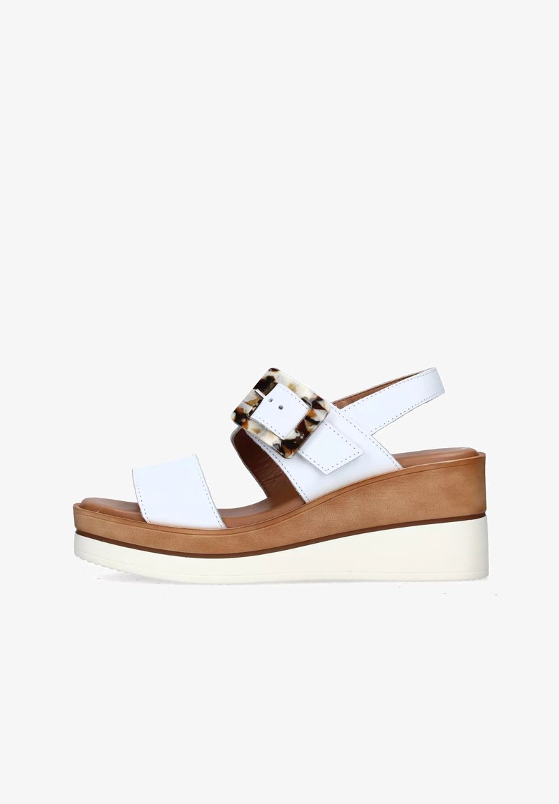 Sandali con zeppa bianchi in pelle liscia, con una grande fibbia in acetato tartarugato e una suola piatta di colore marrone contrastante.