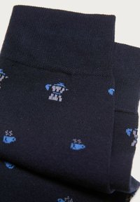 Calzini blu scuro con piccoli motivi di cani e tazze blu chiaro e bianche lavorati nel tessuto, piegati per mostrare il risvolto superiore e i dettagli del design.