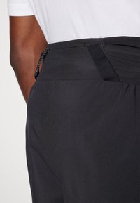 Black athletic trousers featuring a smooth texture, elastic waistband, and adjustable drawstring at the back for a secure fit.