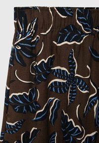 Brown fabric with blue and white leaf patterns. Features an elastic waistband and flowing design. Textured surface with a relaxed fit.