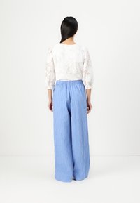 Vit blus i blommönstrad spets med puffärmar, kombinerad med ljusblå, texturerade vida byxor med elastisk midja.