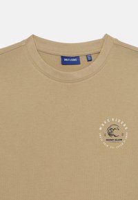 Tan cotton t-shirt with a round neckline. Features a circular graphic print in white and navy with stylized wave design and text on the chest.