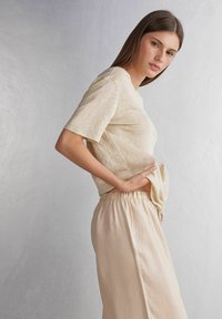 Béžové tričko s krátkým rukávem a volným střihem, vyrobené z měkké, texturované látky. Spárované se světle zbarvenými kalhotami s elastickým pasem.