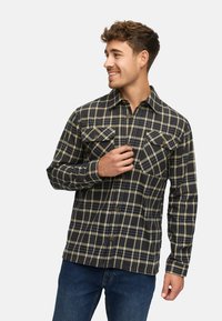 Skjorte i ternet flannel i mørk navy og olivengrøn, med to brystlommer, knaplukning og lange ærmer. Struktureret stofdesign.