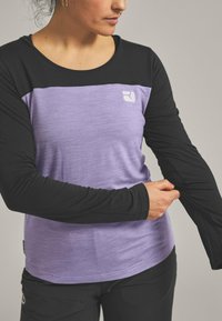 Long-sleeve top featuring a black body and a lilac panel with a subtle texture, round neckline, and a logo on the chest.