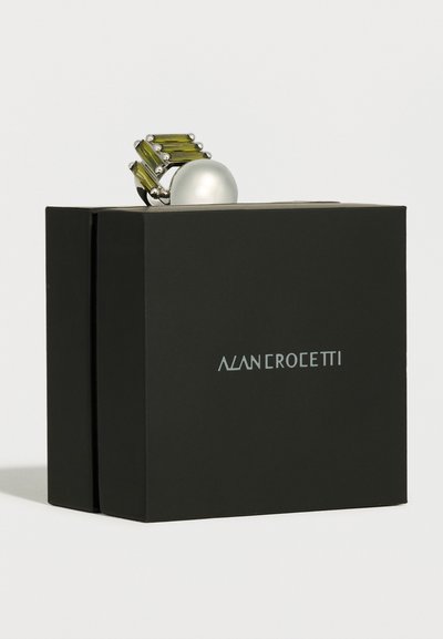 Srebrn prstan z veliko belo biserino in štirimi pravokotnimi zelenimi dragimi kamni, postavljen na črno škatlo Alan Crocetti.