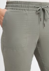 Helle grüne Jogginghosen mit elastischem Bund und Kordelzug, ausgestattet mit seitlichen Taschen und einem weichen, strukturierten Stoff. Akzente umfassen Metallösen.