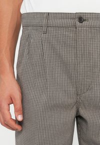 Gray checkered trousers with a waistband and a single button closure, featuring pleats and a smooth texture, highlighting a classic design.