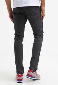 Mustat slim-fit farkut, joissa on viisi taskua, hieman haalistunut pinta ja näkyvät saumat, yhdistettynä harmaisiin ja punaisiin lenkkikenkiin.