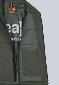 Grünes Steppjackenfutter mit horizontalen Nähten, einem auffälligen weißen Logo, zwei Innentaschen und einem orangefarbenen Etikett.