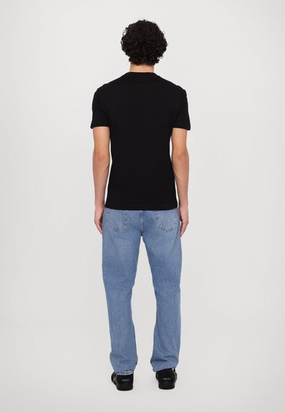 Sort kortærmet t-shirt, parret med lyseblå denimjeans, set fra ryggen. Casual pasform med et enkelt design. Sorte fodtøj.