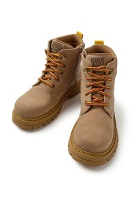 Botines tan con suelas de goma gruesas, cordones amarillos y rojos, cremalleras laterales y etiquetas de marca en la lengüeta, presentados sobre un fondo blanco.