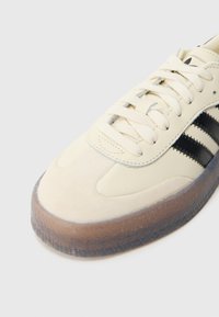 Svářená obuv z béžové kůže s černými pruhy, vybavená semišovou špičkou, strukturovanou mezipodešví a průsvitnou gumovou podrážkou.