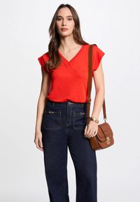 Rode V-hals t-shirt met korte mouwen, gecombineerd met donkerblauwe high-waisted jeans. Bruine handtas met goudkleurige hardware accenten.