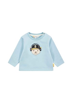 Camiseta de manga larga azul claro con un oso bordado que lleva auriculares y una gorra. Los detalles notables incluyen un botón a presión en el hombro.