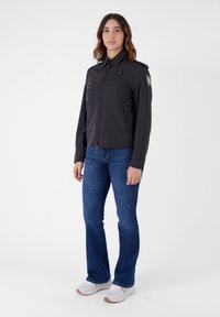 Giacca leggera nera con colletto alto, chiusura a zip e tasche laterali. Abbinata a jeans a zampa d'elefante blu e sneaker bianche.
