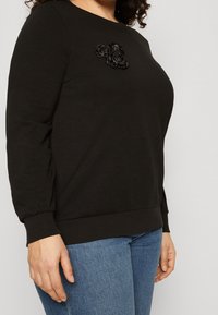 Black sweatshirt made of soft fabric, featuring a round neckline and gathered long sleeves, adorned with black fabric rose appliqué.