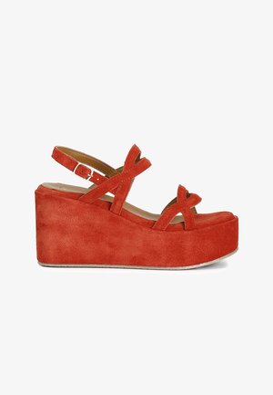 Sandalia de cuña con plataforma de ante rojo, con tiras cruzadas y hebilla ajustable en el tobillo, vista lateral sobre fondo blanco.