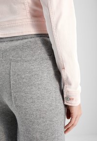 Ljusrosa denimjacka med knäppta ärmslut, tillsammans med grå stickade sweatpants med en bakficka och texturerad tyg.