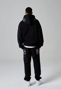 Conjunto de sudadera y pantalones de chándal negros, con acentos gráficos en blanco. Tejido suave, corte relajado y puños acanalados. Zapatillas completan el look.