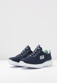 Navy mesh athletic shoes with mint accents and lacing system. White sole features flex grooves for comfort and flexibility.
