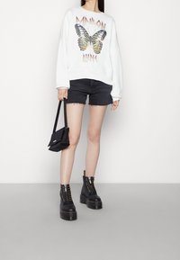 Bílá mikina s barevnou grafikou motýlů, ve spojení s tmavými džínovými šortkami. Černé bojové boty s tlustou podrážkou a malá černá crossbody taška.