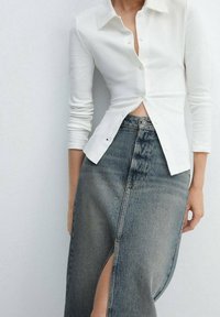 Bílá dlouhá košile s předním zapínáním na knoflíky, spárovaná s vysokým denimovým sukní se bočním rozparkem a světle modrou barvou.