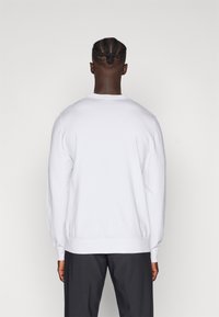 Bílý svetr s crewneck výstřihem a dlouhými rukávy, s žebrovanými manžetami a lemem, měkká texturka, zobrazený zezadu na jednoduchém pozadí.