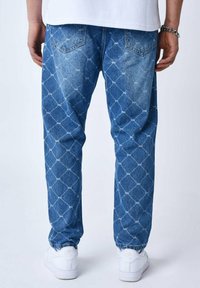 Jeans de mezclilla en azul claro con un patrón de diamantes, que cuentan con un corte relajado y puños elásticos. Combinados con zapatillas blancas.