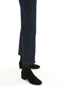 Botas de tobillo de ante negro con un tacón bajo de bloque, llevadas con jeans de mezclilla azul oscuro de corte recto y costuras claras.