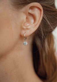 Orecchino a cerchio in argento con un pendente rotondo decorato con un motivo a occhio, dettagliato con linee radiali, appeso a una chiusura sicura.