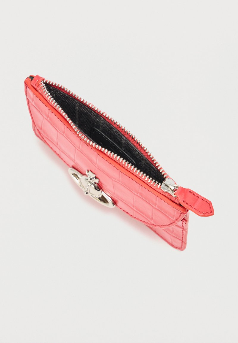 Small coral pink crocodile-patterned leather pouch with silver zipper and oval metal emblem on plain background.