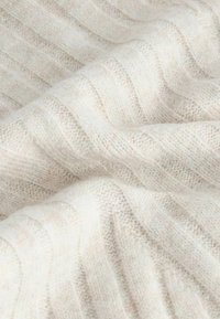 Tissu en tricot doux de couleur crème avec une texture côtelée subtile et des plis délicats.