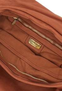 Interno di una borsa in pelle marrone con cerniera dorata e etichetta. Texture liscia, con più scomparti per l'organizzazione.
