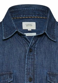 Blå denimskjorte med knapper, spids krave, forlommer og "camel active"-mærke syet indeni halsudskæringen.