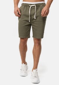 Pantalones cortos de algodón verde oliva con cintura elástica y cordón blanco, con bolsillos laterales y un pequeño detalle de logo en la pierna.