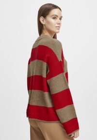 Maglione a righe rosse e beige con una vestibilità morbida, scollatura rotonda e maniche lunghe. Realizzato in morbido tessuto a maglia, presenta bande di colore a contrasto.