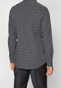 Camisa de manga larga con estampado en blanco y negro, que presenta un diseño de logo repetido, confeccionada en tela lisa, con un ajuste entallado en la parte trasera.