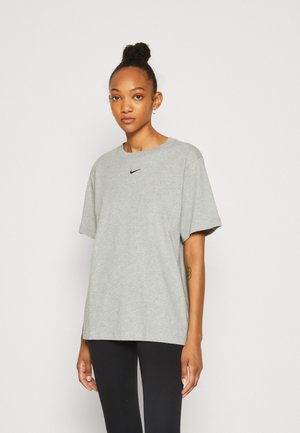 Camiseta de algodón gris con mangas cortas, cuello redondo y un logotipo negro de Nike en el pecho, combinada con leggins negros.