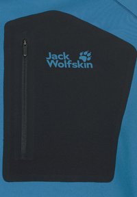 Blauer Fleece-Oberteil mit einem schwarzen Brustpaneel, einem Reißverschlussfach und einem blauen "Jack Wolfskin"-Logo. Glatte Textur mit kontrastierenden Farben.